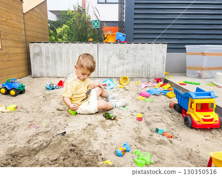 Child playing alone in a sandbox with toys on a playground, enjoying outdoor activities Child playing alone in a sandbox with toys on a playground, enjoying outdoor activities 130350516