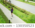 Young woman walking with a small white dog on a leash along a paved path  130350523