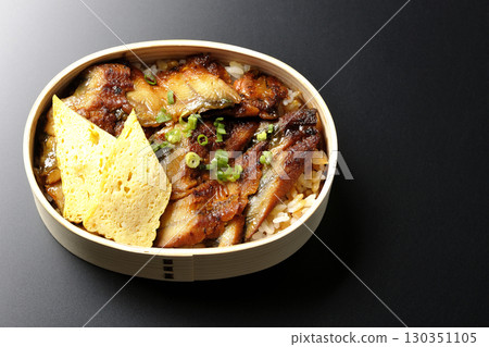 Eel bowl bento in a bento box photographed against a black background 130351105