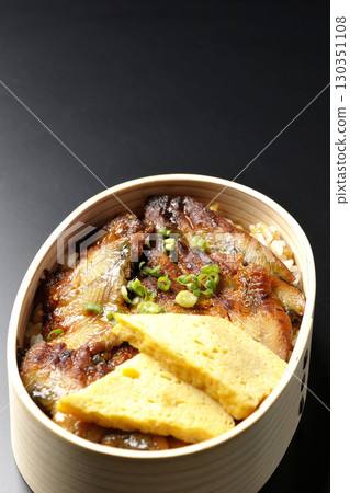 Eel bowl bento in a bento box photographed against a black background 130351108