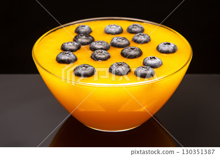 Bright mango dessert topped with fresh blueberries served in a clear bowl 130351387