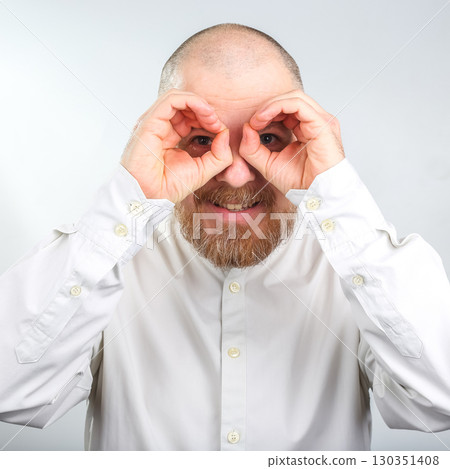 Man making binoculars with hands, smiling, and engaging in playful gesture indoors Man making binoculars with hands, smiling, and engaging in playful gesture indoors 130351408
