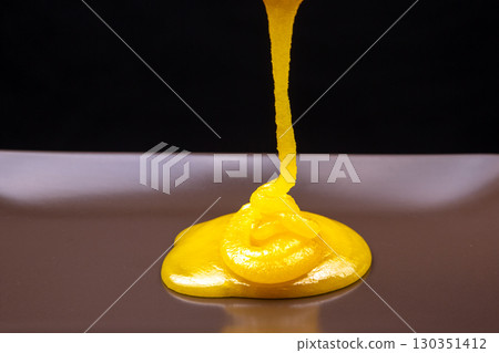 Yellow condiment flowing onto a sleek surface in a creative culinary presentation Yellow condiment flowing onto a sleek surface in a creative culinary presentation 130351412