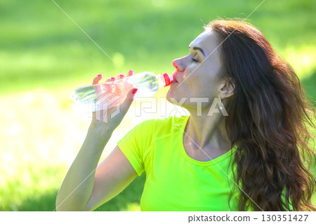 Woman enjoying refreshing water in bright green park during sunny day 130351427