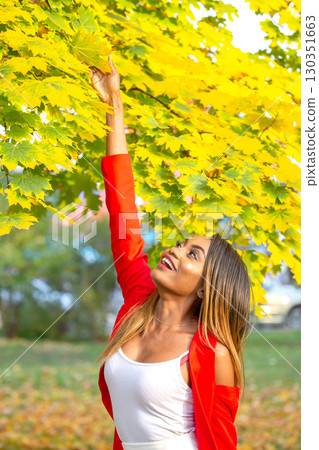 African woman reaching for bright yellow leaves in a sunny park during autumn African woman reaching for bright yellow leaves in a sunny park during autumn 130351663