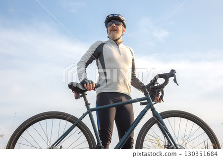 Cyclist posing confidently with bike against a clear sky during sunrise Cyclist posing confidently with bike against a clear sky during sunrise 130351684