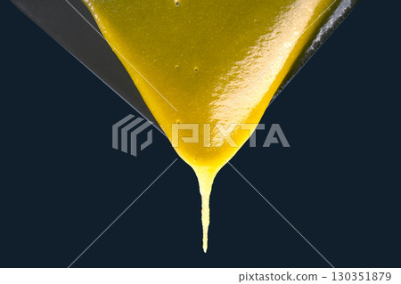 Golden liquid dripping from a spoon, showcasing its thick and smooth texture in a dark setting Golden liquid dripping from a spoon, showcasing its thick and smooth texture in a dark setting 130351879