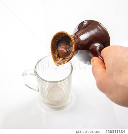 Pouring handmade coffee from a ceramic jug into a glass cup at a cozy kitchen Pouring handmade coffee from a ceramic jug into a glass cup at a cozy kitchen 130351884