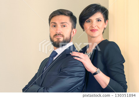 Professional couple poses confidently against a neutral background in a casual business setting 130351894