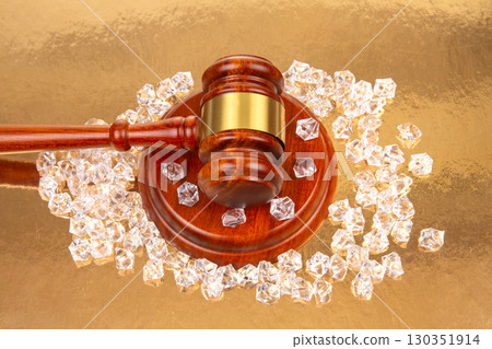 Legal gavel surrounded by sparkling gems on a reflective golden surface 130351914