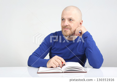 Man with beard reading a book and thinking in a bright room during daytime 130351916