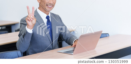 Senior businessman using a computer and making a peace sign 130351999
