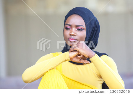 Thoughtful African woman in black hijab and yellow outfit poses outdoors in natural light 130352046