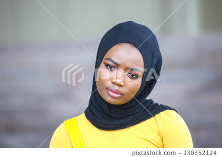 Confident African woman poses in modern attire with traditional headscarf in urban setting 130352124