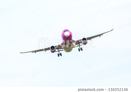 Airplane approaches landing at an airport on a cloudy day with a pink and yellow design 130352136