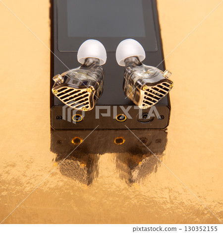 High-end audio equipment with transparent earbuds resting on a golden surface 130352155