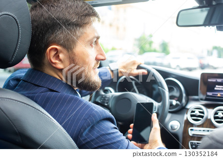Man in a suit driving a car while using a smartphone in a busy urban environment Man in a suit driving a car while using a smartphone in a busy urban environment 130352184