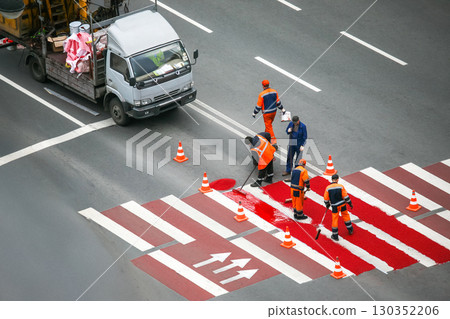 Workers paint new red pedestrian crosswalk on busy city street during daytime 130352206