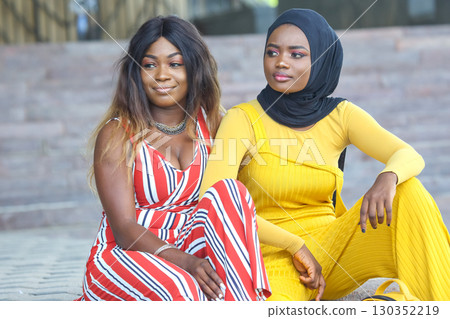 Two African women posing together outdoors in colorful outfits at a modern urban location 130352219