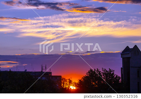 Colorful sunset over urban skyline with clouds and trees visible in the background Colorful sunset over urban skyline with clouds and trees visible in the background 130352316