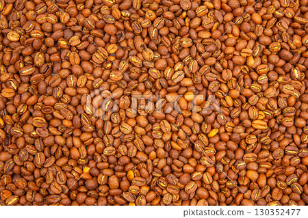 Roasted coffee beans spread out on a surface, showcasing rich color and texture 130352477