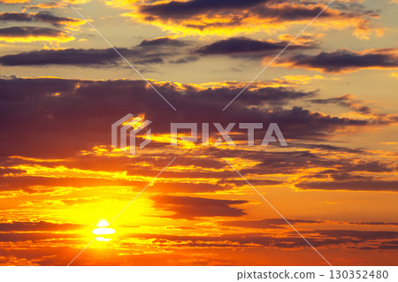 Vibrant sunset casts golden hues across dramatic cloud formations in the evening sky 130352480