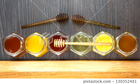 Various jars of honey with honey dipper arranged on a wooden surface in a kitchen setting Various jars of honey with honey dipper arranged on a wooden surface in a kitchen setting 130352481