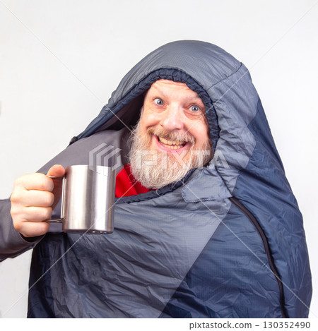 Cozy man wrapped in sleeping bag enjoying warm drink indoors during winter season 130352490