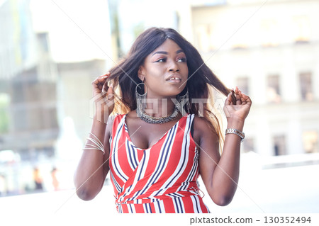 African woman posing confidently in a stylish red-striped dress outdoors 130352494