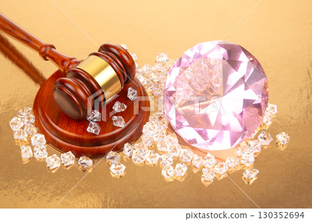 Gavel beside large pink gem and smaller diamonds on shiny surface during auction event 130352694