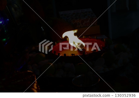 An oil lamp burning with a strong flame in the dark, radiating spiritual energy during puja rituals. 130352936