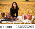 A woman wearing a black ribbed knit sweater and a plaid skirt enjoying a picnic in an autumn park 130353205