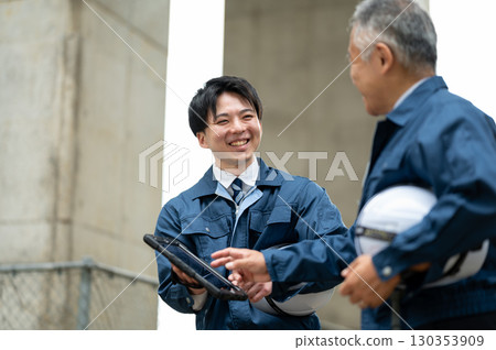 A young and experienced engineer conversing at a construction site 130353909