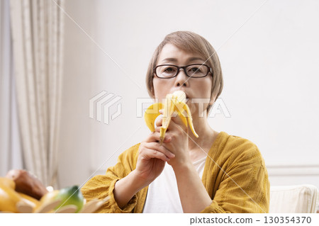 Senior woman peeling and eating a banana in the dining room 130354370
