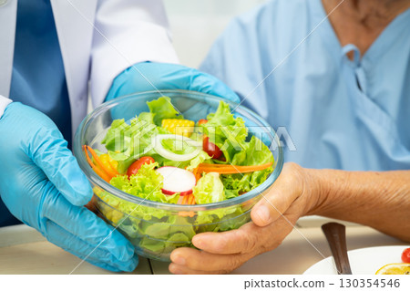 Asian elderly woman patient eating breakfast with vegetable and fruit healthy food while sitting  in hospital. 130354546