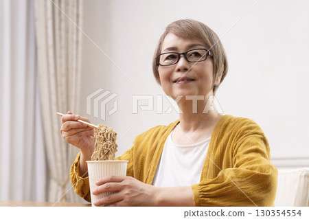 Senior woman eating instant noodles in the dining room Senior woman eating instant noodles in the dining room 130354554