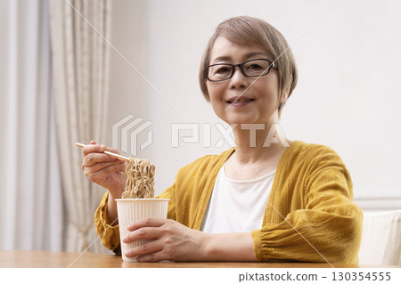 Senior woman eating instant noodles in the dining room Senior woman eating instant noodles in the dining room 130354555