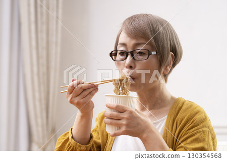 Senior woman eating instant noodles in the dining room Senior woman eating instant noodles in the dining room 130354568