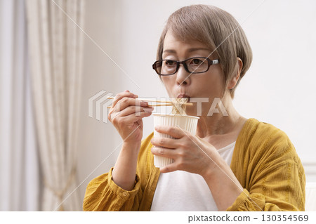 Senior woman eating instant noodles in the dining room Senior woman eating instant noodles in the dining room 130354569