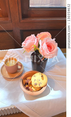 Coffee cup, cookie bowl, pink rose vase resting on white tablecloth beside window, radiating warm, intimate morning moment Coffee cup, cookie bowl, pink rose vase resting on white tablecloth beside window, radiating warm, intimate morning moment 130354632