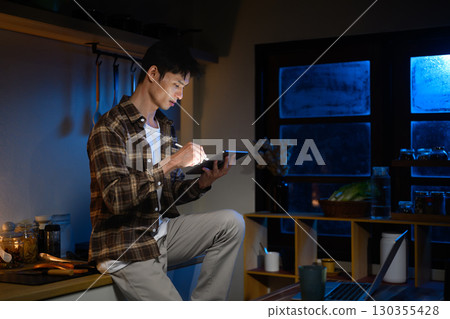 Asian man working overtime from home, writing on digital tablet with stylus 130355428