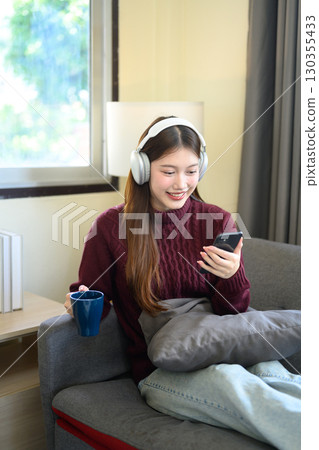Cheerful woman enjoying music with headphones while browsing her smartphone Cheerful woman enjoying music with headphones while browsing her smartphone 130355433