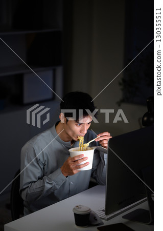 Overworked employee eating instant noodles at desk while working late at night 130355511