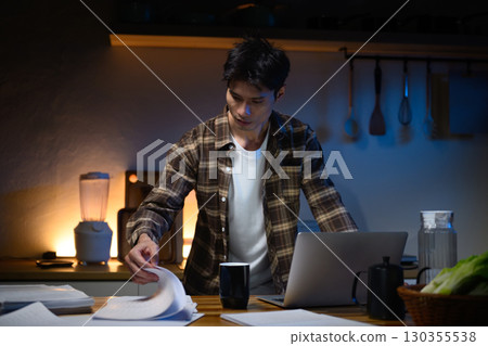 Msn working overtime in a kitchen, focused on paperwork under warm evening light 130355538