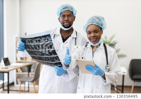 Confident male and female doctors collaborate using patient scans and digital tablets. Health professionals showcase teamwork, expertise promoting medicine, diagnostics, progress. Confident male and female doctors collaborate using patient scans and digital tablets. Health professionals showcase teamwork, expertise promoting medicine, diagnostics, progress. 130356495