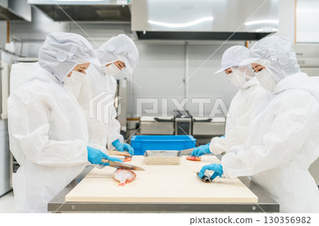 Male and female staff in sanitary clothing preparing fish (chef, cook, fresh market, food processing) Male and female staff in sanitary clothing preparing fish (chef, cook, fresh market, food processing) 130356982