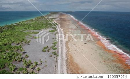French Polynesia, Rangiroa island: Aerial view capturing Tiputa motu's road dividing Rangiroa lagoon and Pacific Ocean, featuring vibrant corals and white sand beaches. Drone flight 130357954
