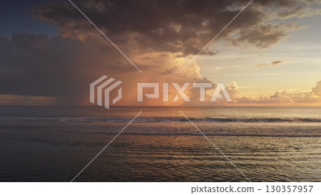 Tropical rain is falling on the ocean at sunset in Tahiti, with colorful clouds and waves gently breaking on the shore, creating a serene and beautiful scene 130357957