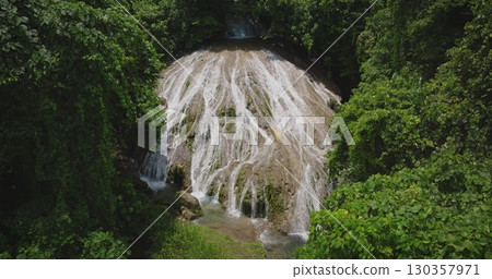 Fiji, Port Villa: Aerial drone of stunning cascade waterfall flowing through a vibrant tropical green rainforest on Efate Island. Vanuatu. Wild nature landscape, travel background. Fiji, Port Villa: Aerial drone of stunning cascade waterfall flowing through a vibrant tropical green rainforest on Efate Island. Vanuatu. Wild nature landscape, travel background. 130357971