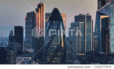 United Kingdom, London: Aerial view of London's financial district at sunset, featuring modern skyscrapers and iconic landmarks against a vibrant sky. Drone flight 130357974